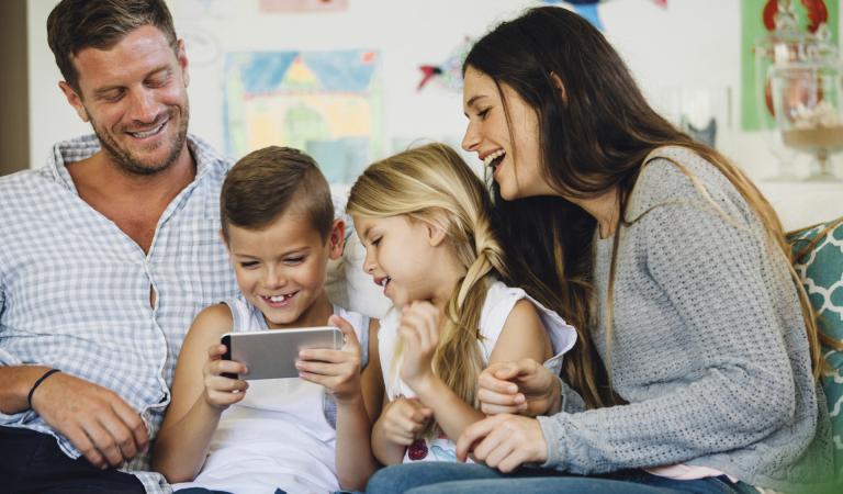 Kids playing on the smart phone surrounded by their parents on the couch